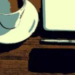 彼女の机の上に置かれた黒いiphoneとコーヒーカップとノートPC